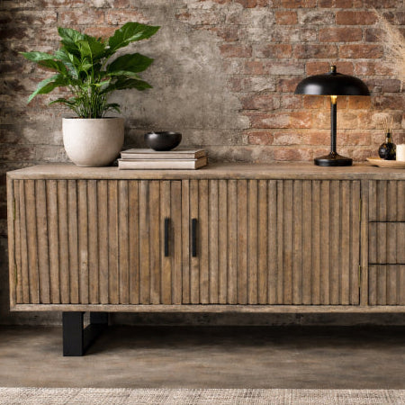 Wooden sideboard with decorative items against a brick wall